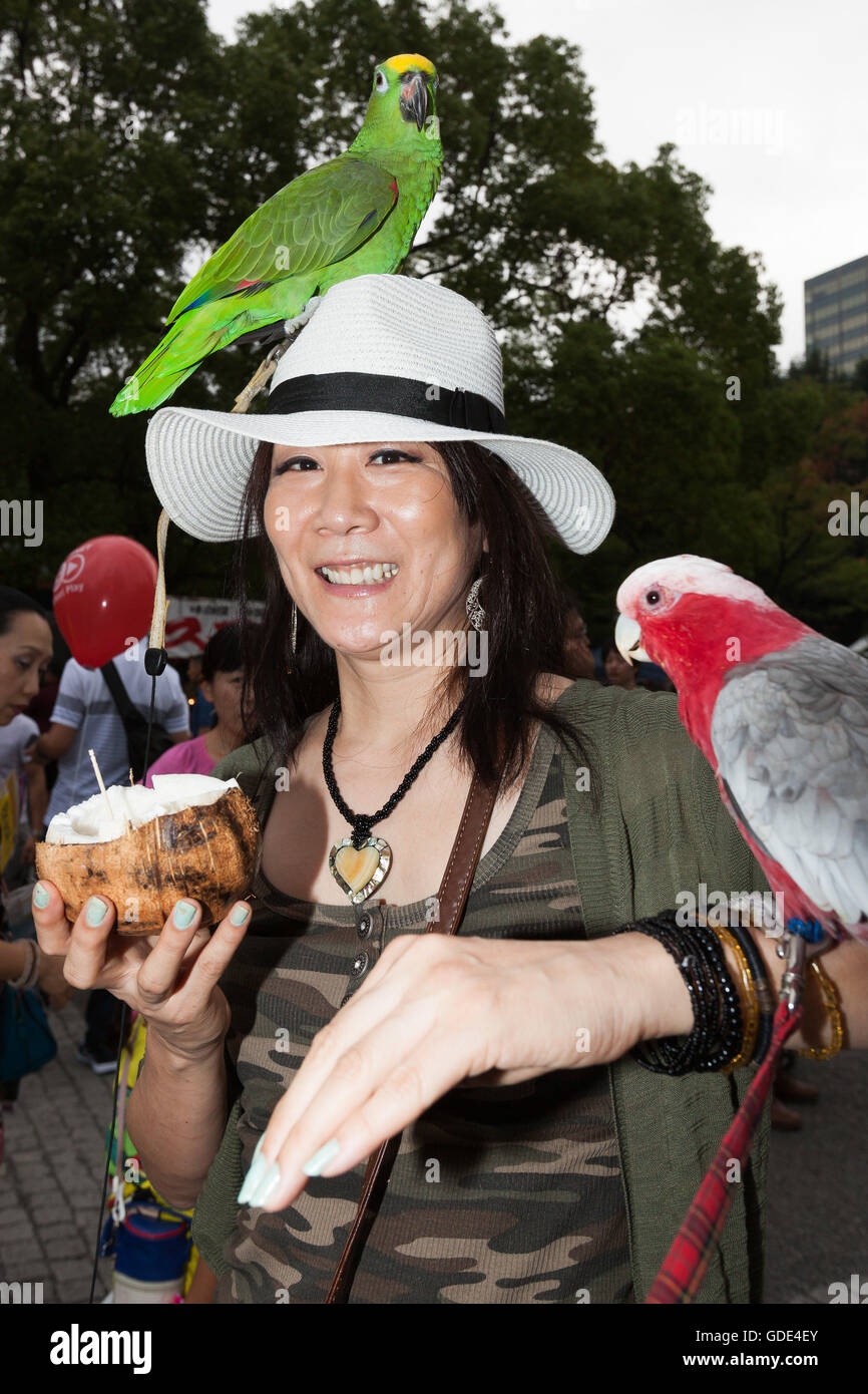 Tokyo, Japan. 16th July, 2016. A woman poses for a photograph with parrots at the Festival Brasil 2016 at Yoyogi Park on July 16, 2016, Tokyo, Japan. The annual festival brings together Brazilian food and entertainment including Samba and Capoeira performers. Organized by the Camara de Comercio Brasileira no Japao the event runs until July 17. The Brazilian community is the third largest immigrant population in Japan. Credit:  Rodrigo Reyes Marin/AFLO/Alamy Live News Stock Photo