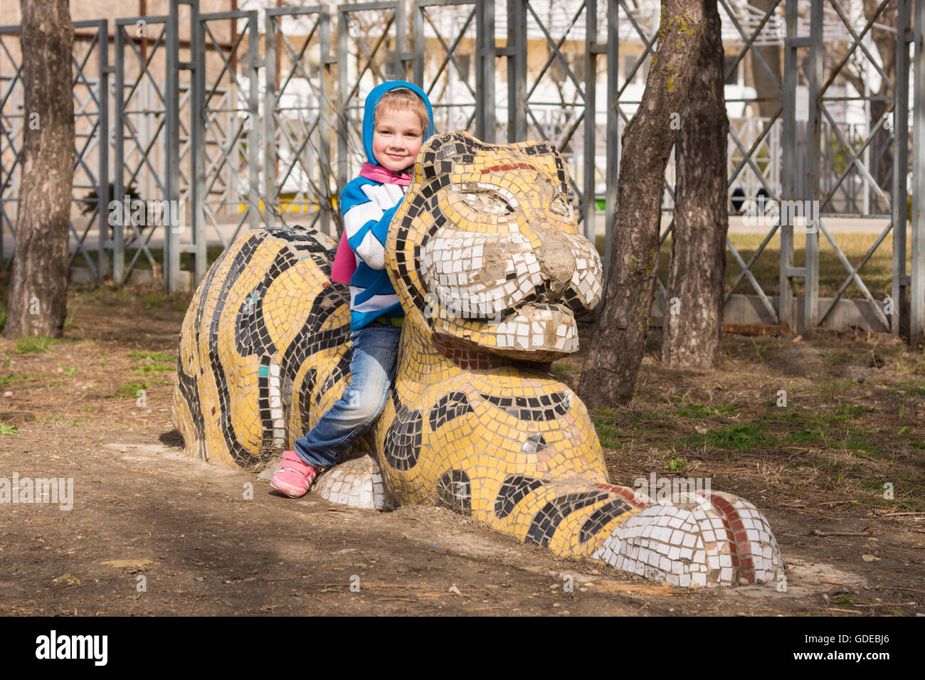 Happy girl sitting on a sculpture of a tiger on the playground in Anapa Stock Photo