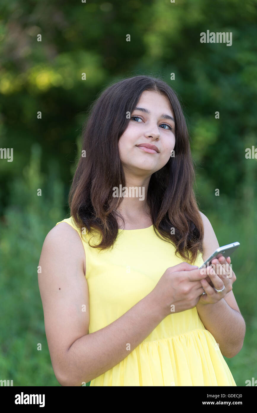 14 year girl holding cell phone and looking up pensively Stock Photo