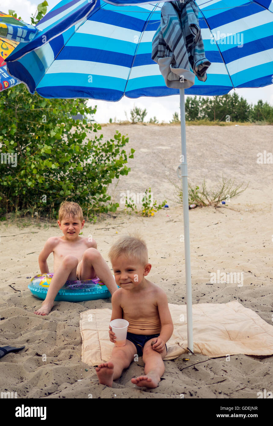 Two boys on the beach sitting under sun umbrella Stock Photo
