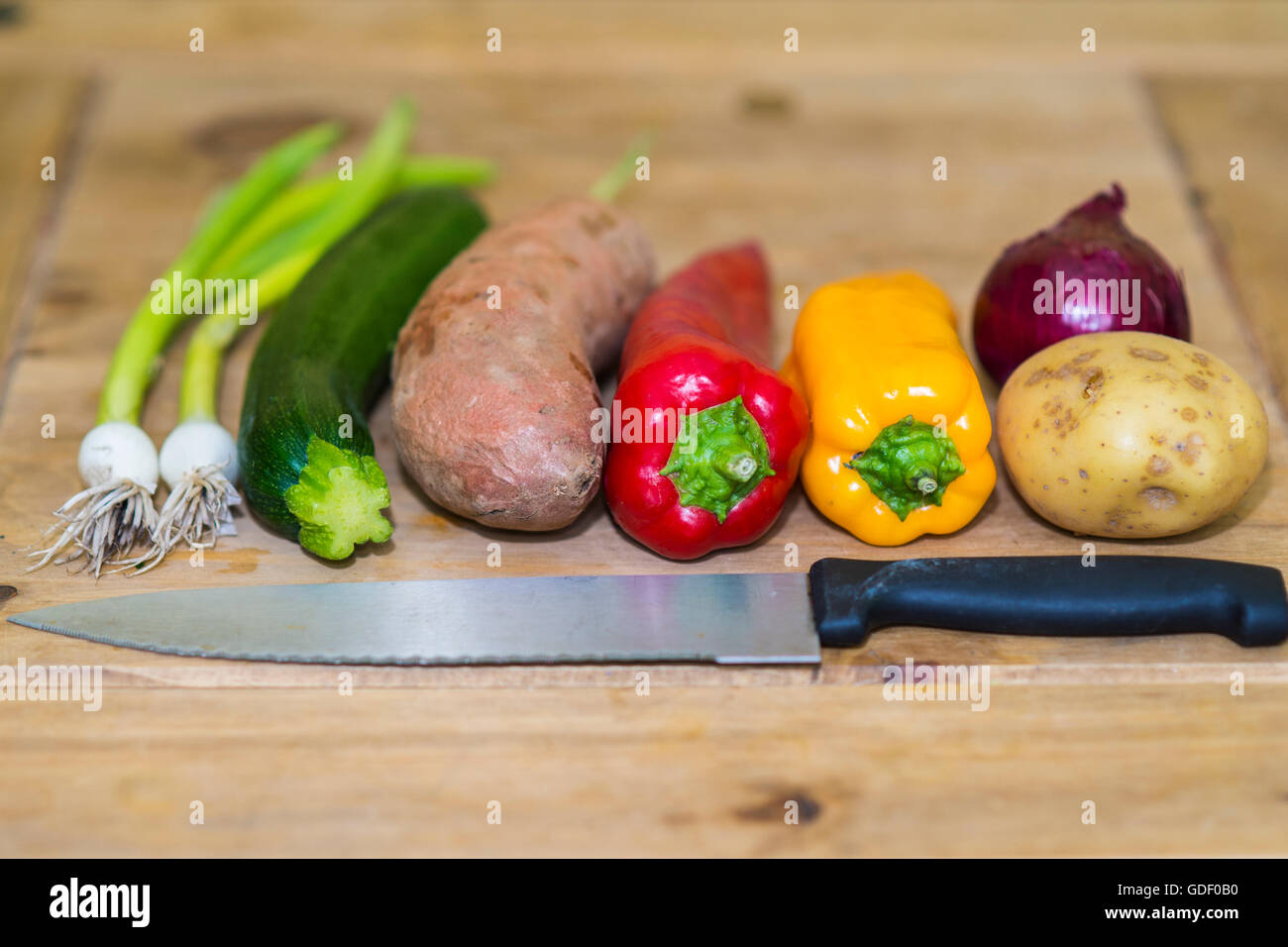 a colourful (colorful) mix of vegetables on a wooden board with a knife Stock Photo