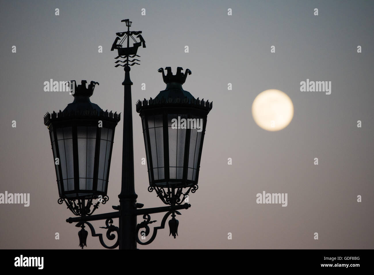 LISBON, Portugal - Silhouette of a street light on Praça do Comércio, with the full moon in the background. Known as Commerce Square in English, Praça do Comércio is an historic square in the Pombaline Downtown district of Lisbon, next to the Tagus River. Stock Photo