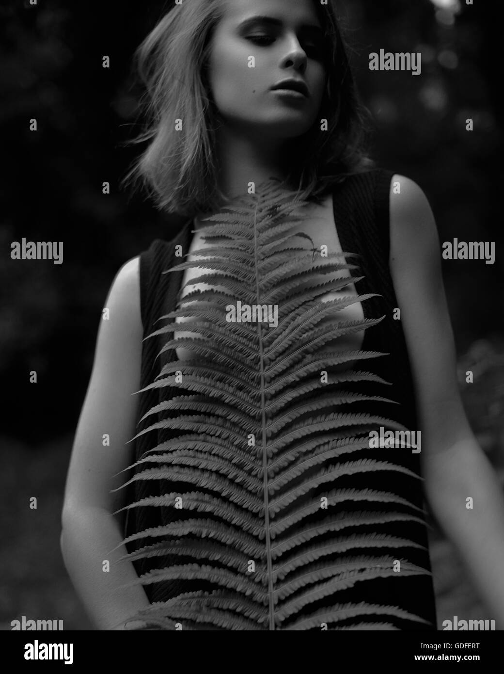 Black and white photo of young dreaming girl with closed eyes in wild plants on summer day holding green fern leaf. Stock Photo