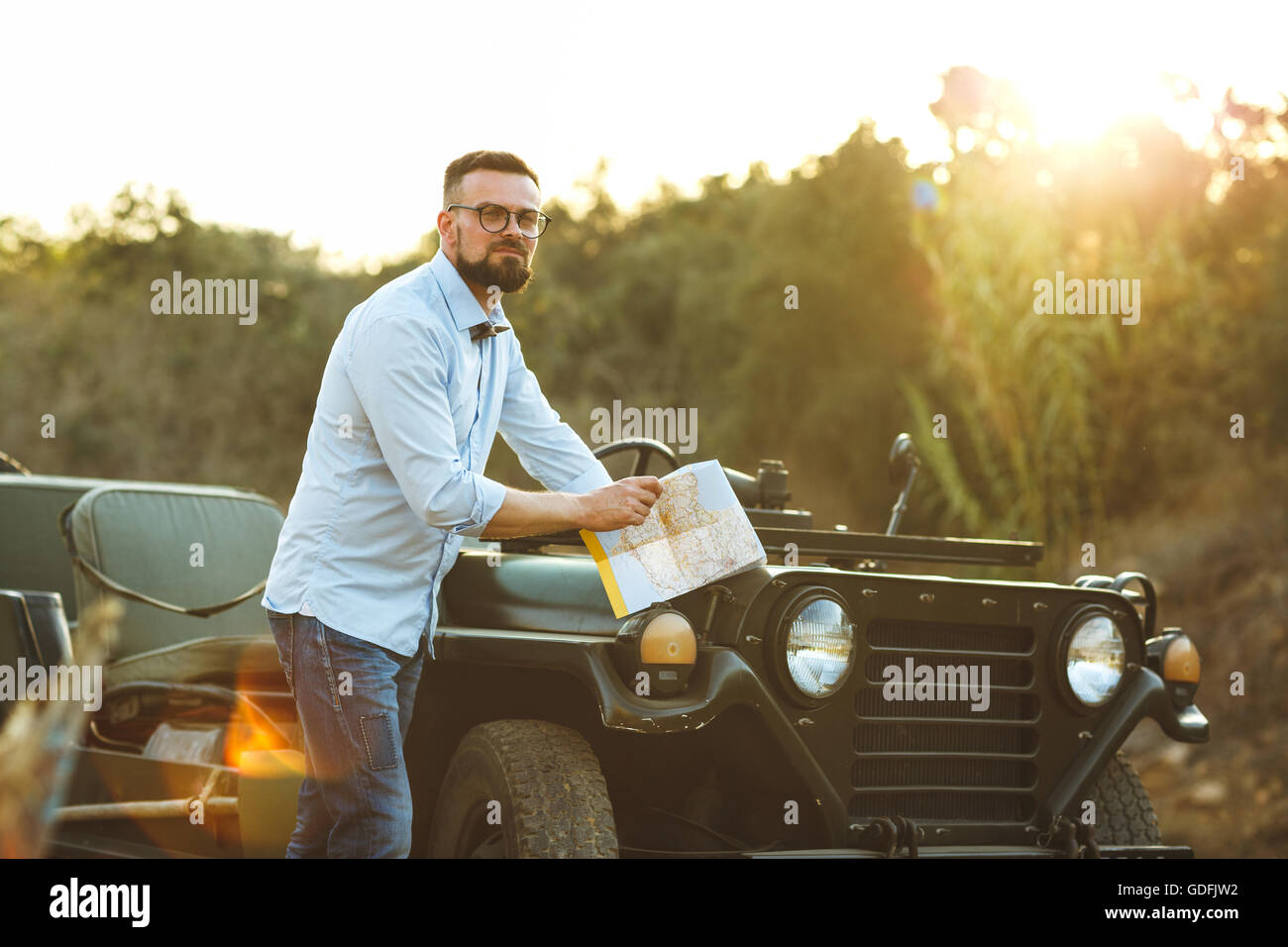 Young stylish man with glasses and bow tie see the map near the old-fashioned SUV on the sunset Stock Photo