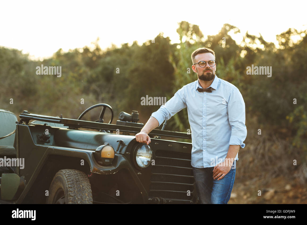Young stylish man with glasses and bow tie near the old-fashioned SUV on the sunset Stock Photo