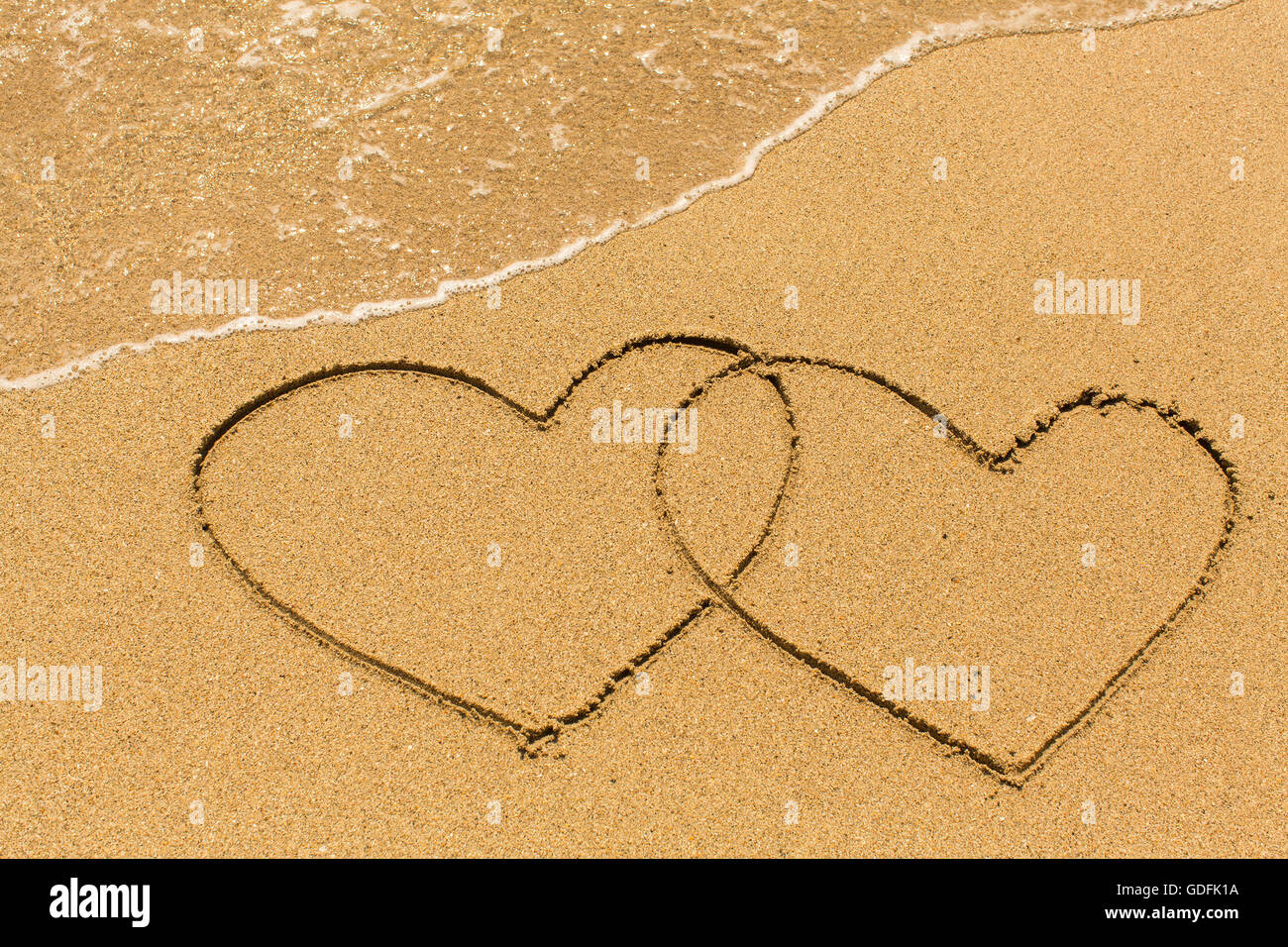 Two of hearts drawn on a sandy beach in the line of sea surf. Stock Photo