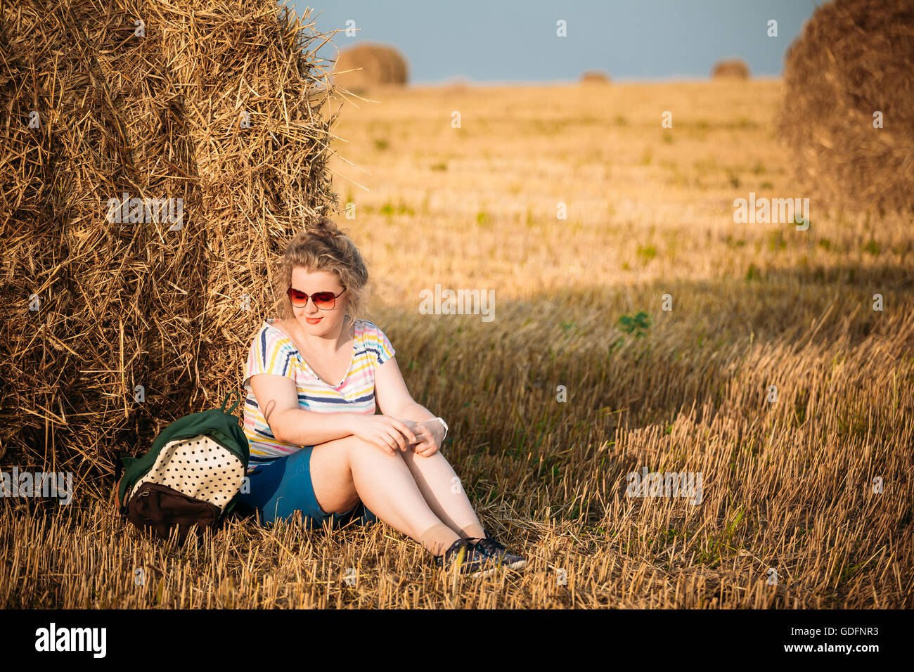 Beautiful Plus Size Young Woman In Shirt Sit Near Hay Bales In Summer Field Meadow At Blue Sly Background Stock Photo