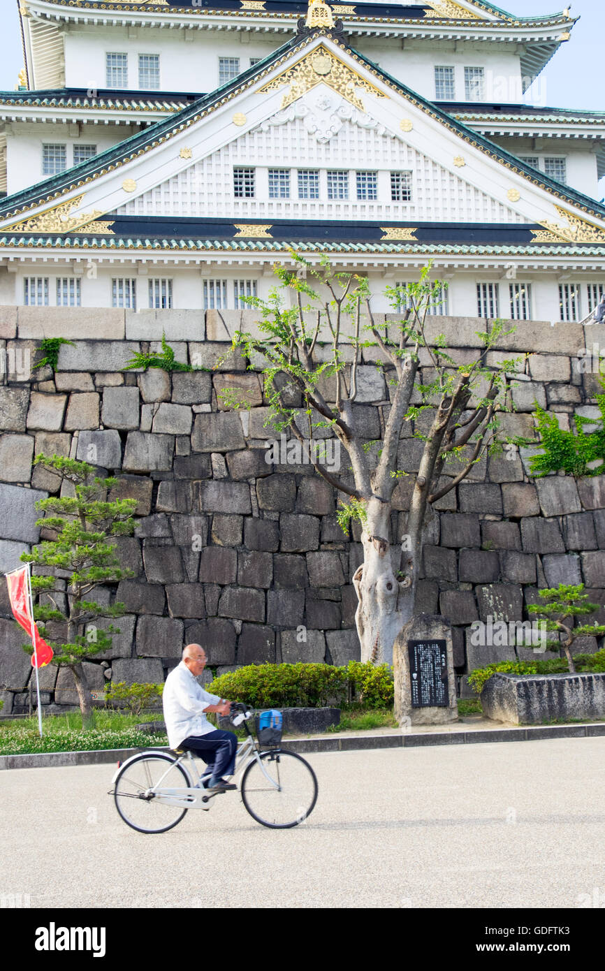 An elderly Japanese man cycling in the grounds of the Osaka Castle. Stock Photo