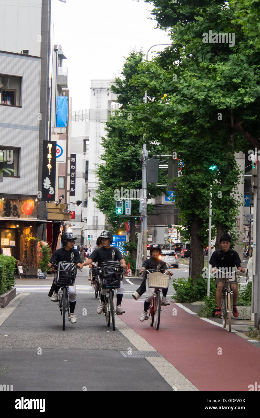 Young boys in baseball uniforms riding their bicycles on on the pavement in downtown Osaka. Stock Photo