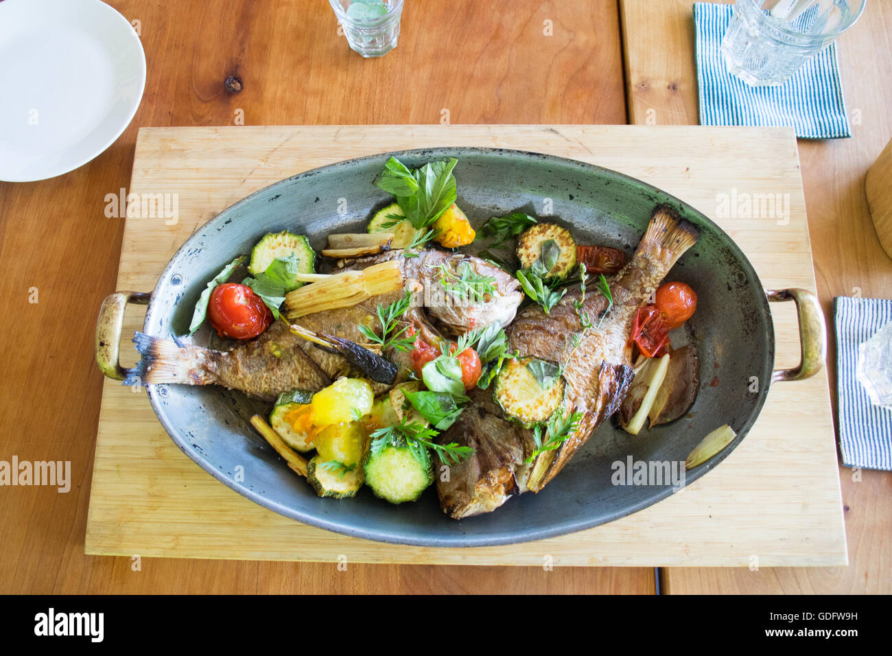 Two roasted fish served with roasted vegetables. Stock Photo