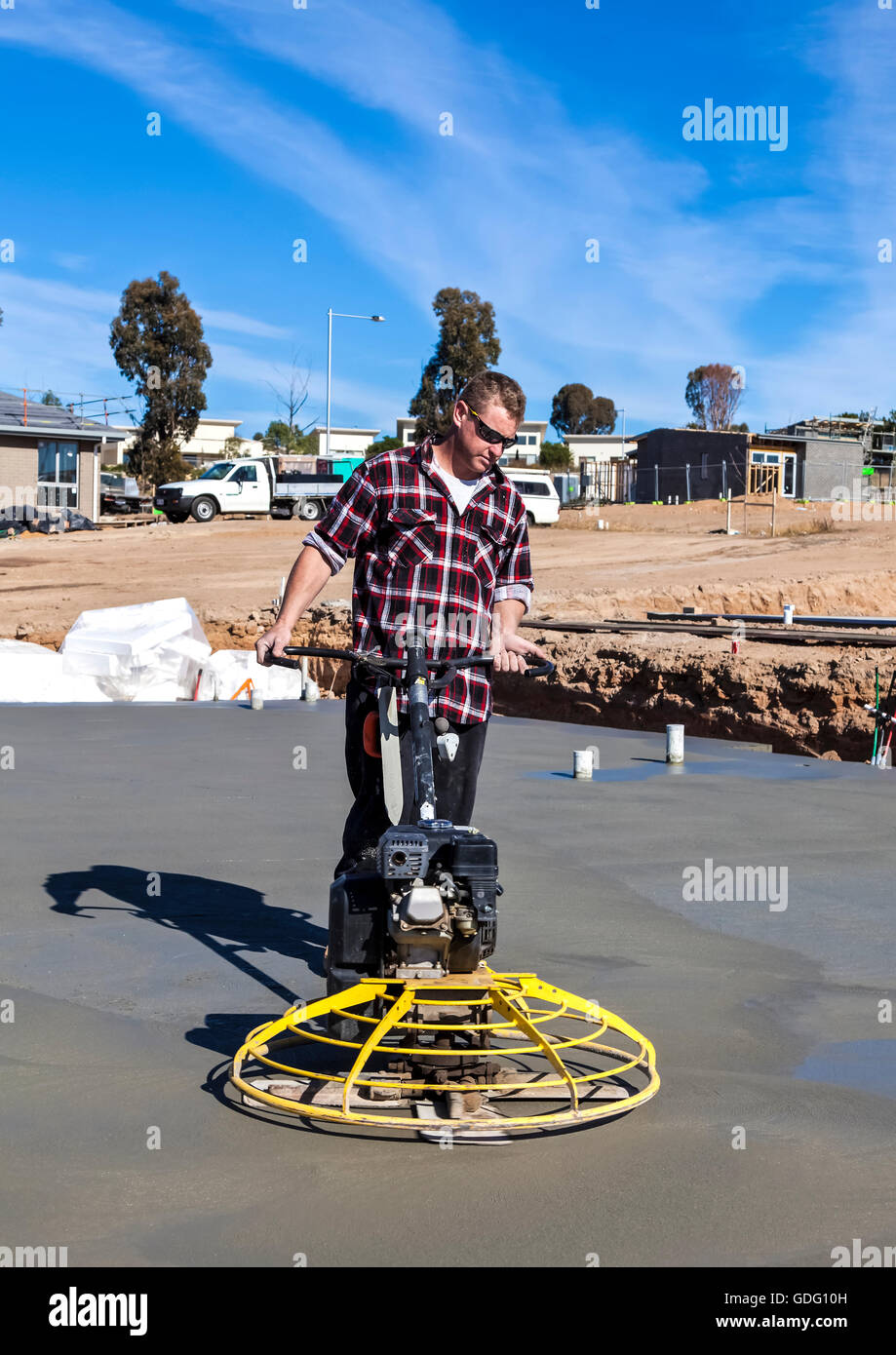 Workman using 'helicopter' concrete smoothing machine on newly poured flooring at housing estate Stock Photo