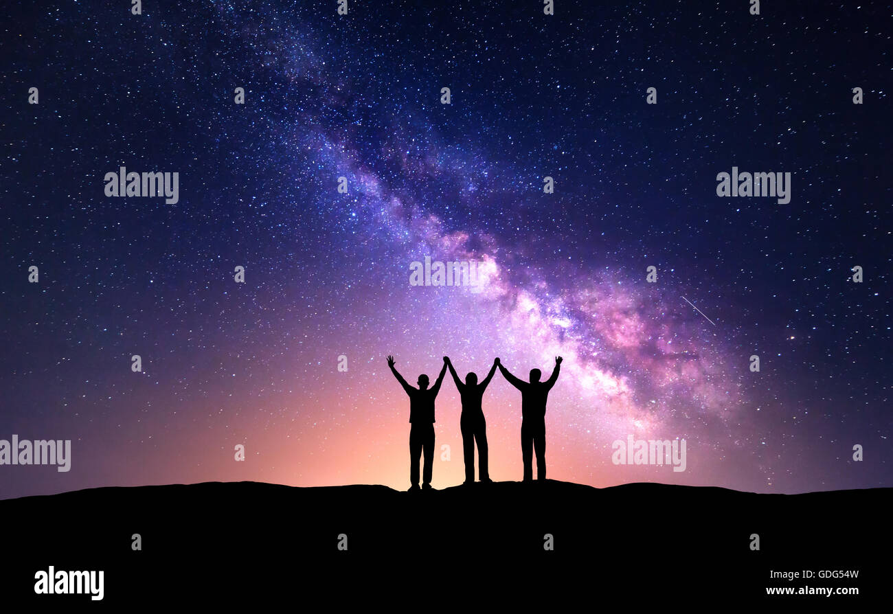 Night landscape with Milky Way and silhouette of people. Night starry sky with silhouette of happy friends with raised-up arms o Stock Photo