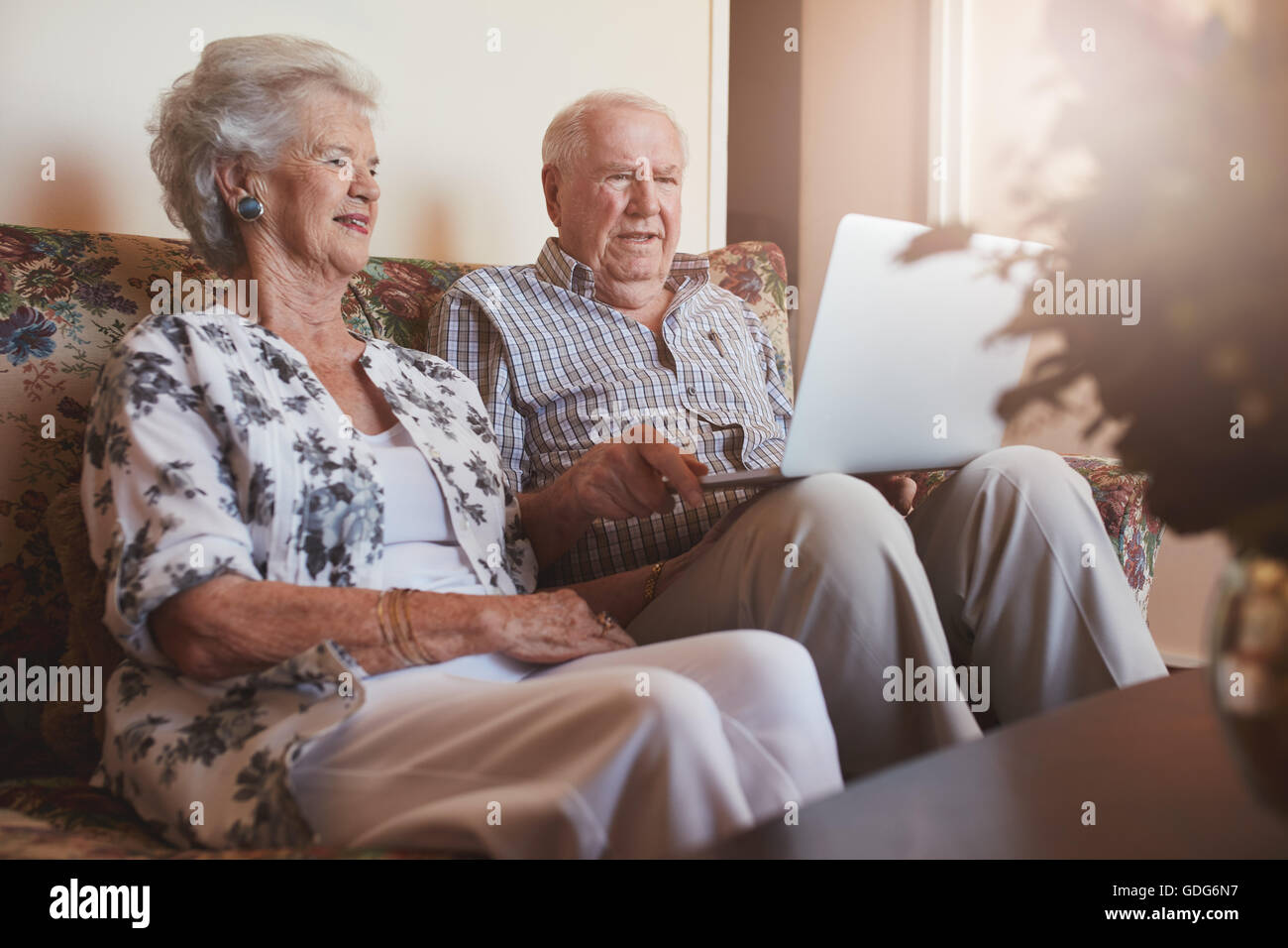 Portrait of happy senior couple sitting together and using laptop computer. Stock Photo