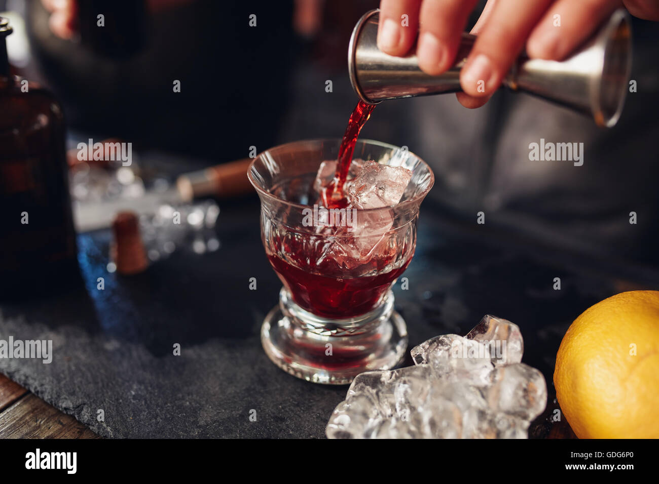 Close up shot of bartender hand pouring drink from measuring cup into a cocktail glass filled with ice cubes. Barman preparing f Stock Photo