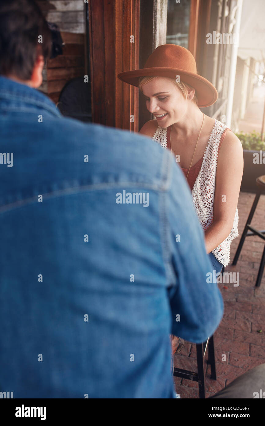 Young caucasian woman wearing hat sitting at a coffee shop with her male friend. Young friends sitting at a cafe table. Stock Photo