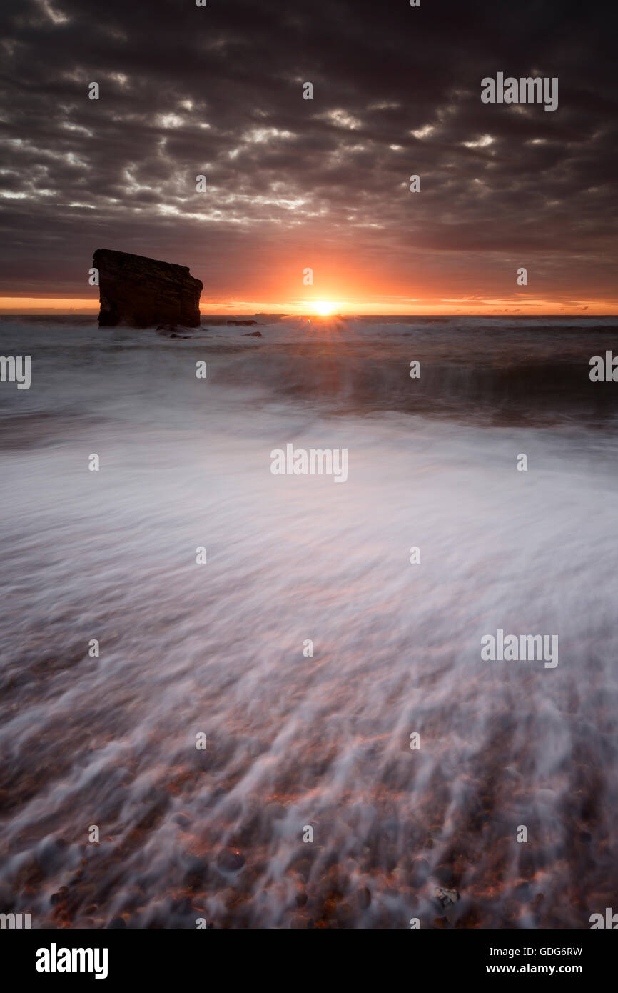 Sunrise behind Charlie's Garden, a sea stack at Seaton Sluice, Collywell Bay Stock Photo