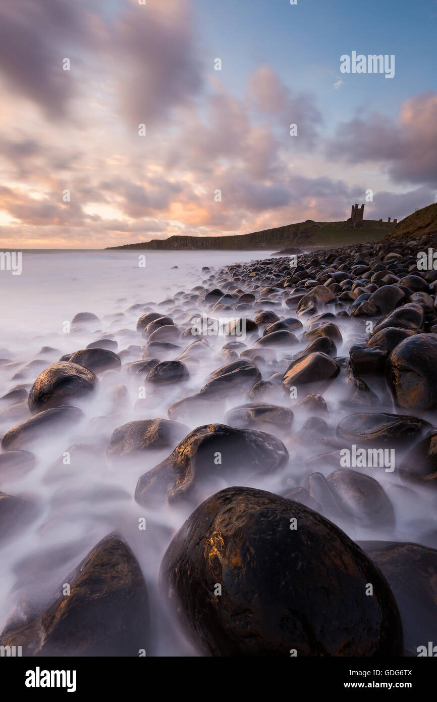 Puffy clouds above Dunstanburgh Castle as the sun rises, Northumberland Stock Photo