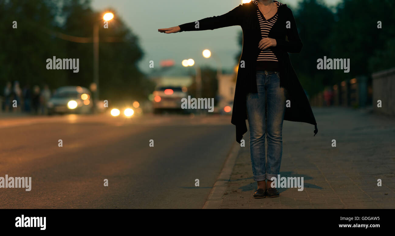 young woman tries to catch a car on night road Stock Photo