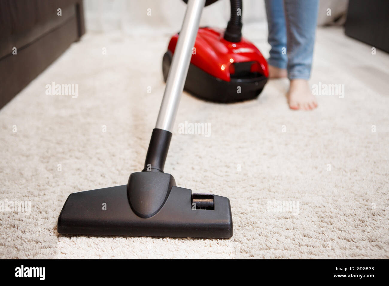 Image of female foot, red vacuum cleaner and black head of vacuum cleaner closeup Stock Photo