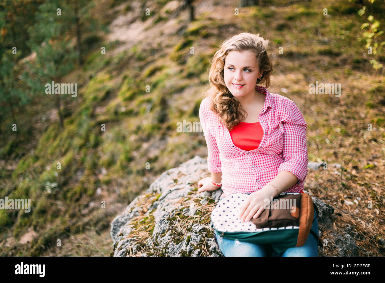 Beautiful Plus Size Young Smiling Woman In Pink Shirt Sitting on Stone in Summer Forest Stock Photo