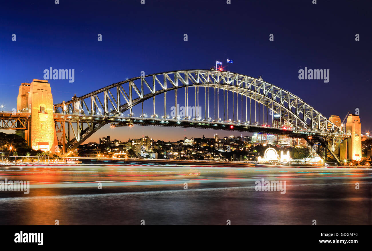 Side view of Sydney Harbour bridge architectural landmark at sunset. Illuminated arch of the bridge reflecting in blurred waters Stock Photo