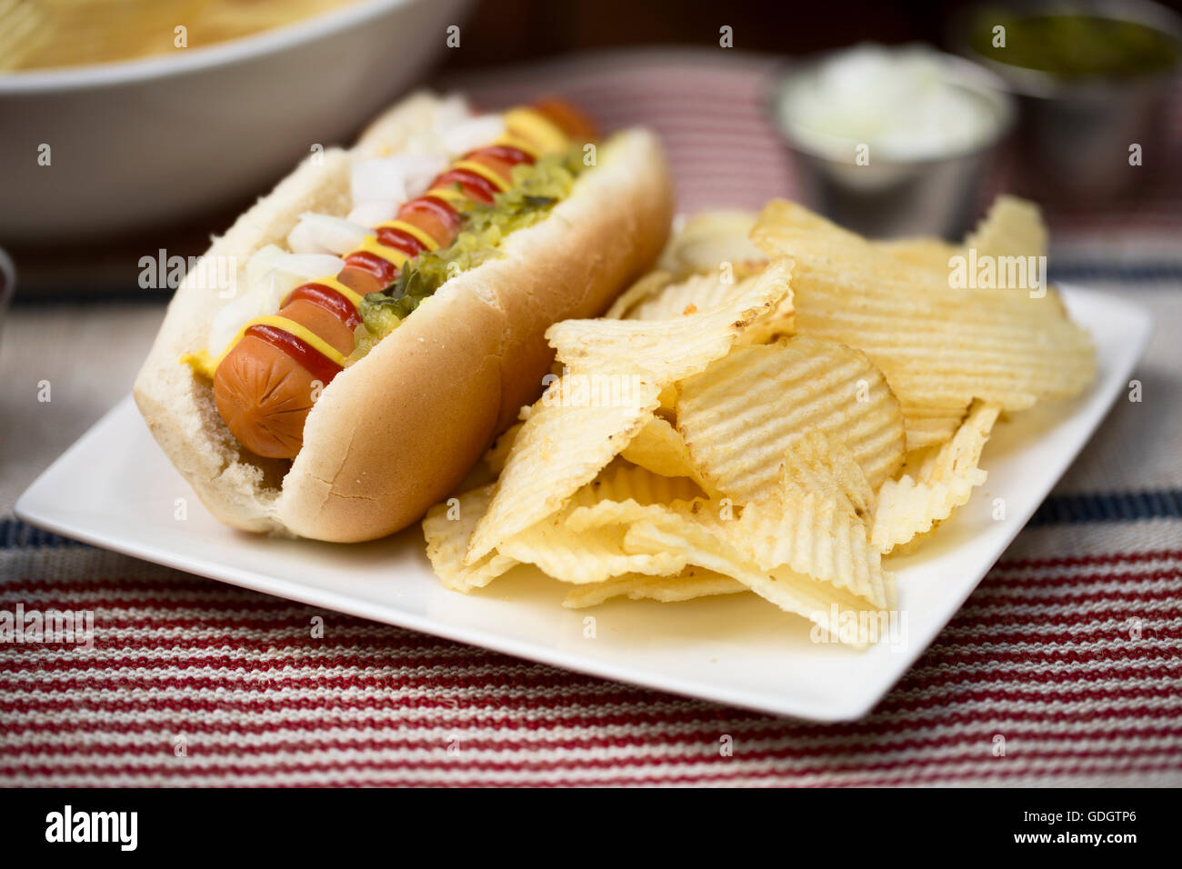 Veggie hot dog topped with mustard, ketchup, onions and relish, served with potato crisps (chips). Stock Photo