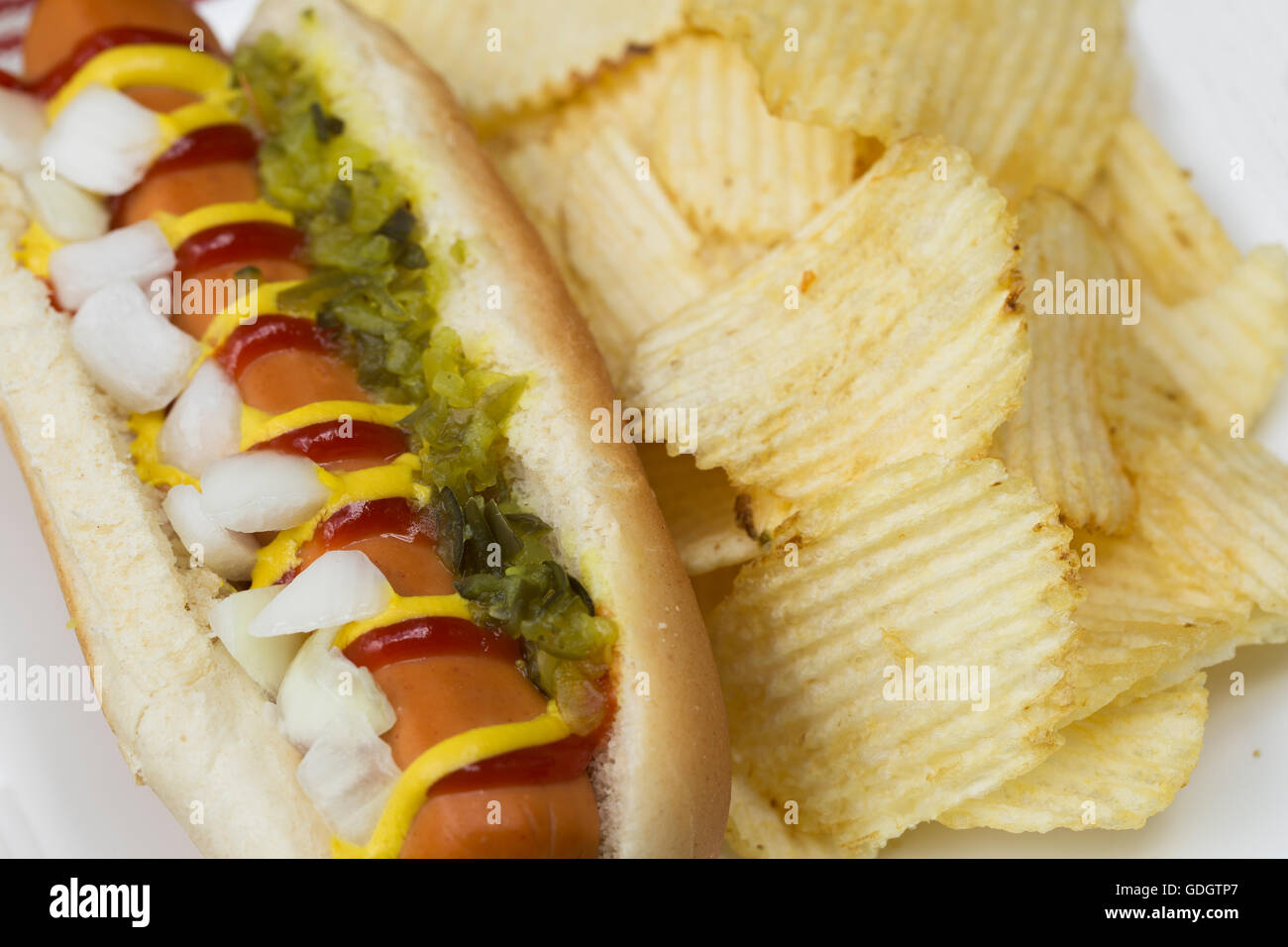 Veggie hot dog topped with mustard, ketchup, onions and relish, served with potato crisps (chips). Stock Photo