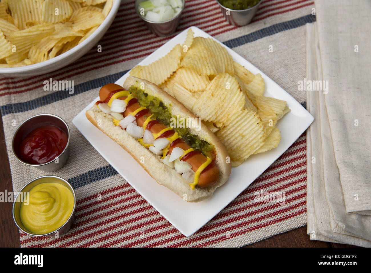 Veggie hot dog topped with mustard, ketchup, onions and relish, served with potato crisps (chips). Stock Photo