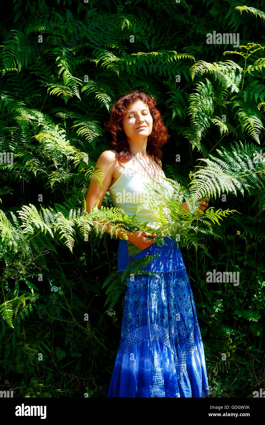 red haired dreaming hippie girl in wild bracken plants on summer day. Stock Photo