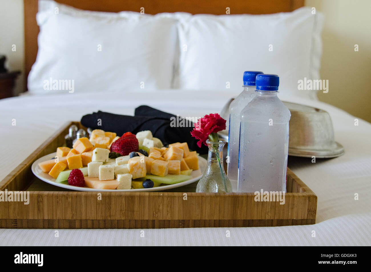 Room service tray on bed in hotel room with fruit and cheese with water