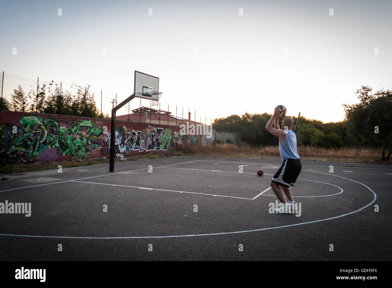 Basketball player in city playground at sunset Stock Photo