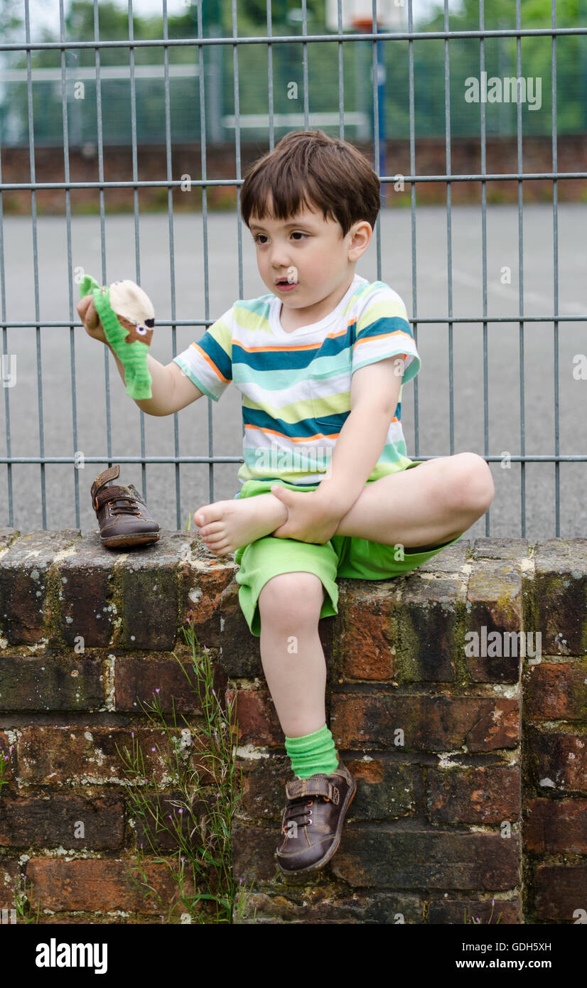 A Young Boy Sits On A Brick Wall To Remove A Stone Form His Shoe Stock 