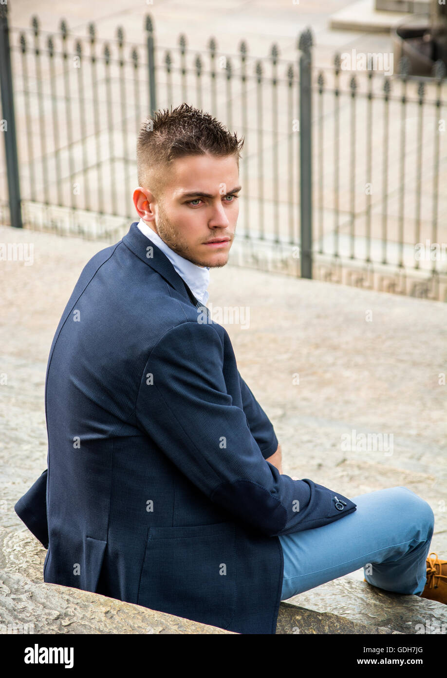 Handsome young man outdoor wearing jacket and shirt sitting by historic ...