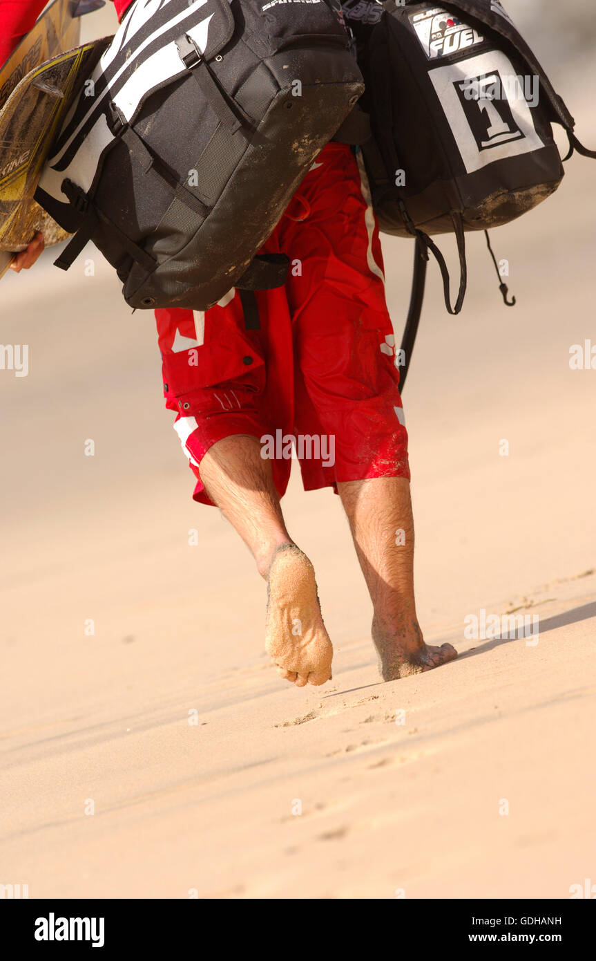 Kite surfer carrying bags of gear down the beach Stock Photo Alamy