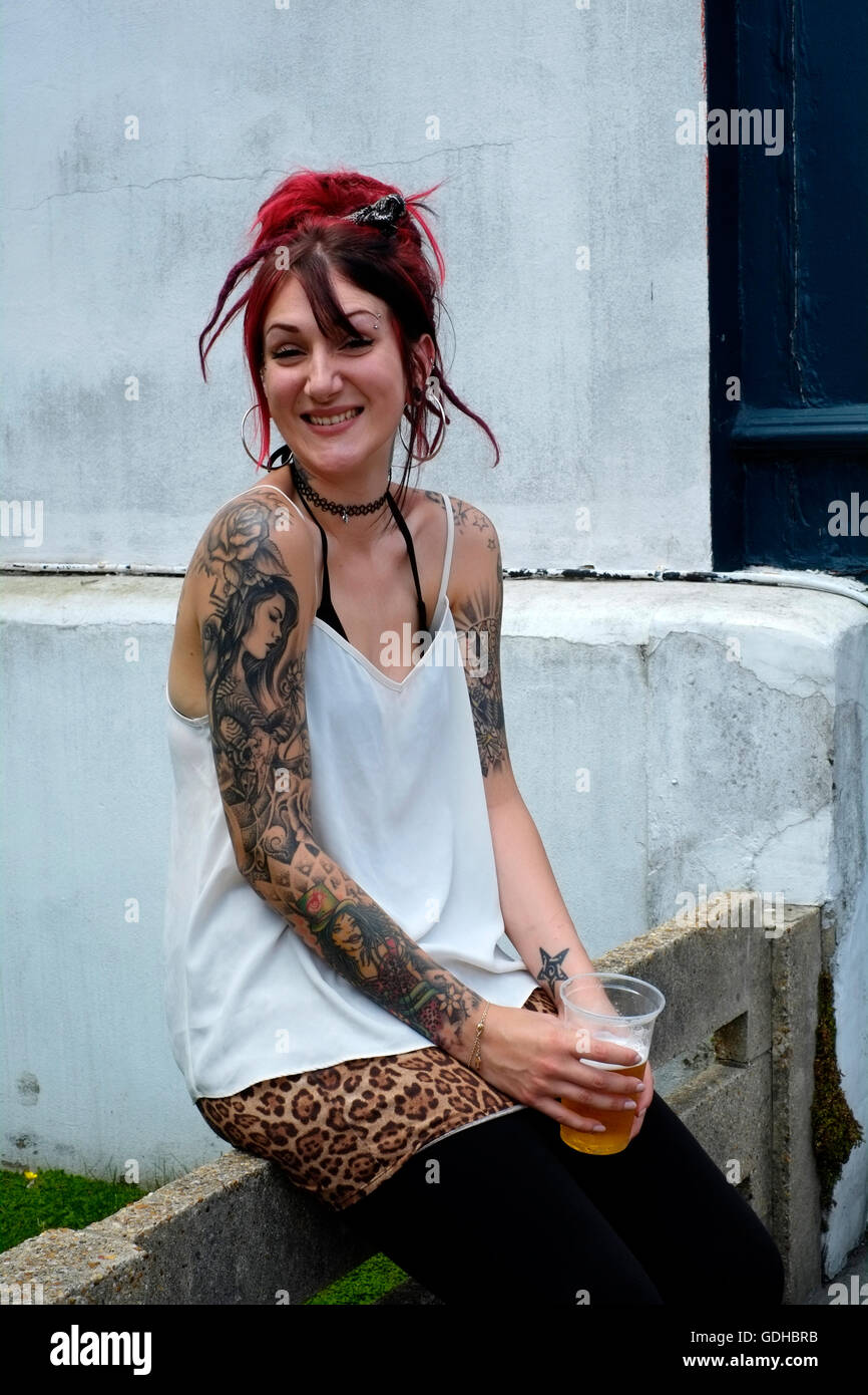a young pretty smiling tattooed female with her hair dyed red holding a beer poses for a portrait in southsea england uk Stock Photo