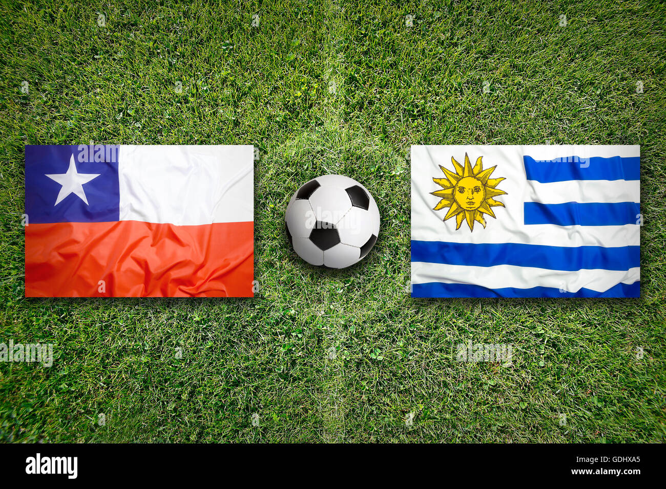 Chile vs. Uruguay flags on green soccer field Stock Photo