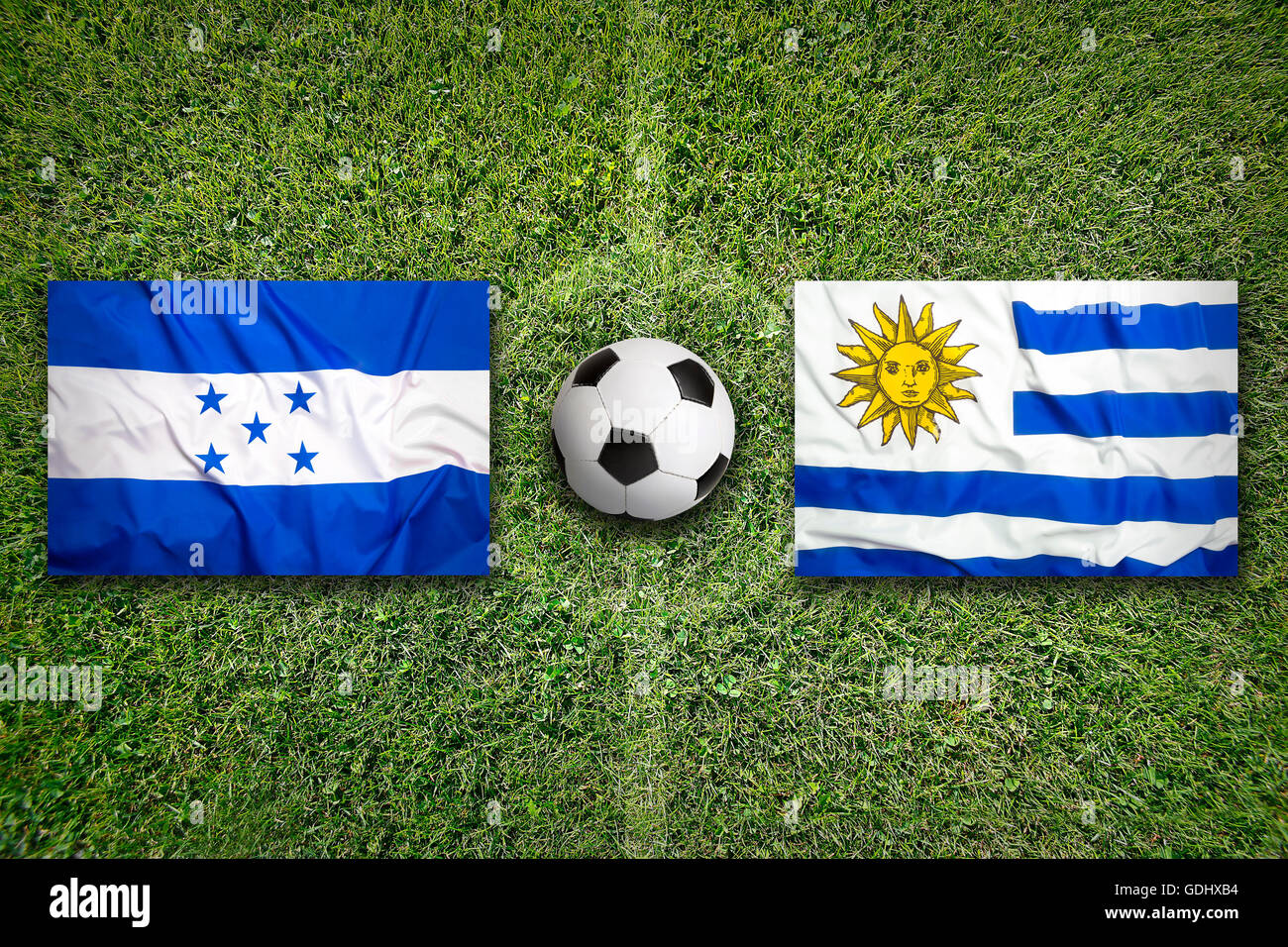 Honduras vs. Uruguay flags on green soccer field Stock Photo