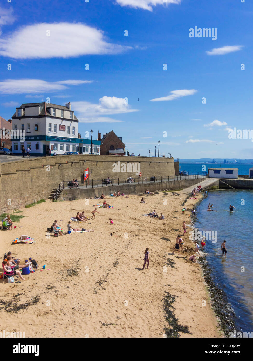 Holidaymakers on the beach by the sea wall at Hartlepool Headland in front of The Pot House pub Stock Photo