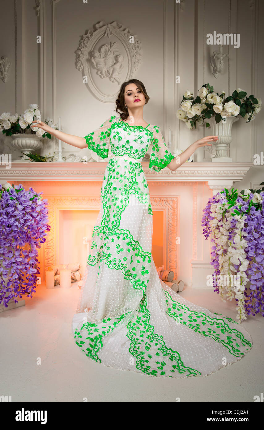 Beautiful lady dressed luxury dress with a train standing in elegant interior decorated of natural flowers. Stock Photo