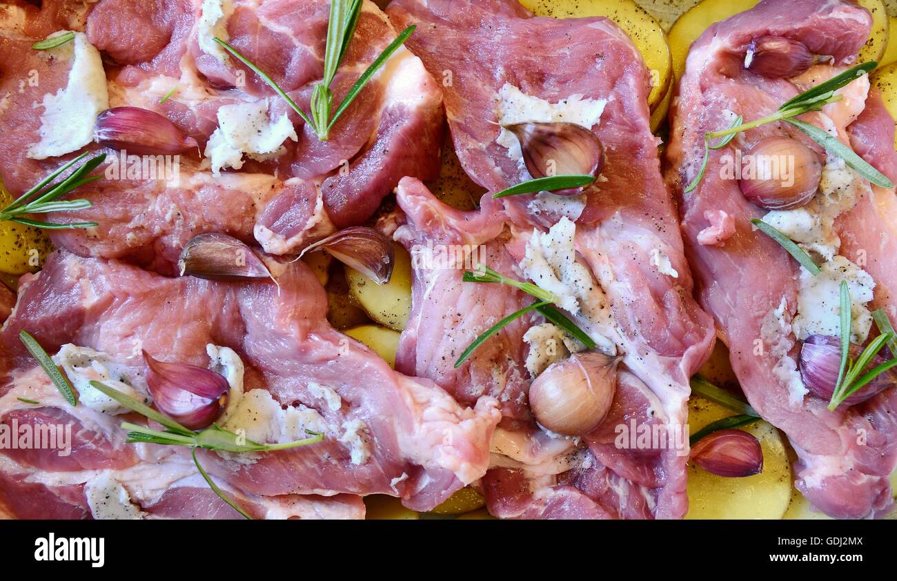 Raw pork neck chops with potatoes slices, rosemary and garlic in pan. The meal is prepared for baking. Stock Photo