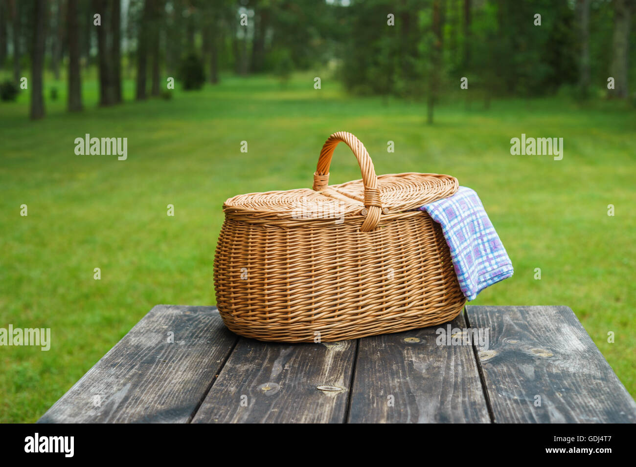 Picnic basket with blue white checkered tablecloth on wooden table. Summertime weekend break concept Stock Photo