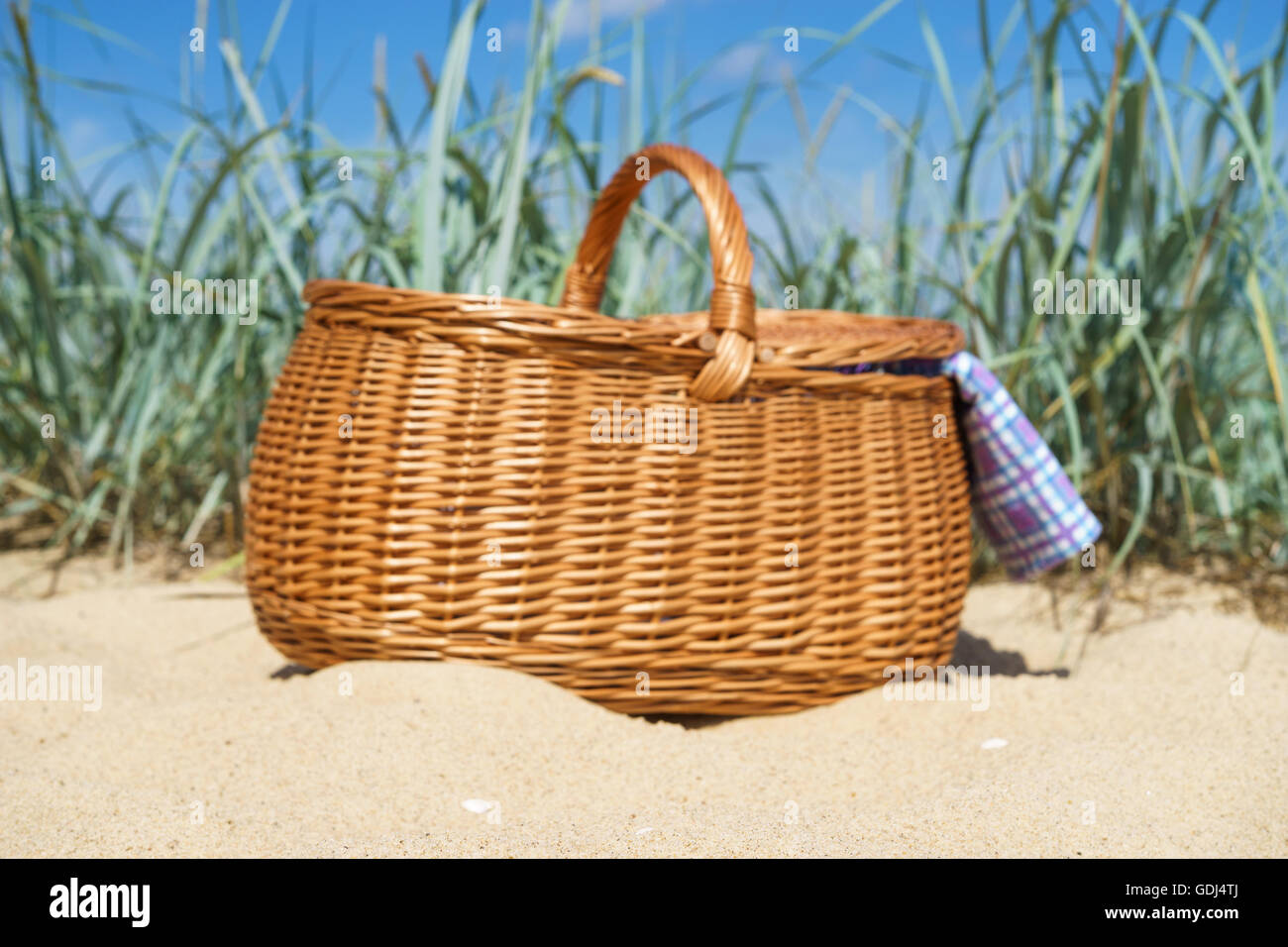 Blurred image of picnic basket with blue white checkered napkin on sandy beach. Weekend break concept Stock Photo