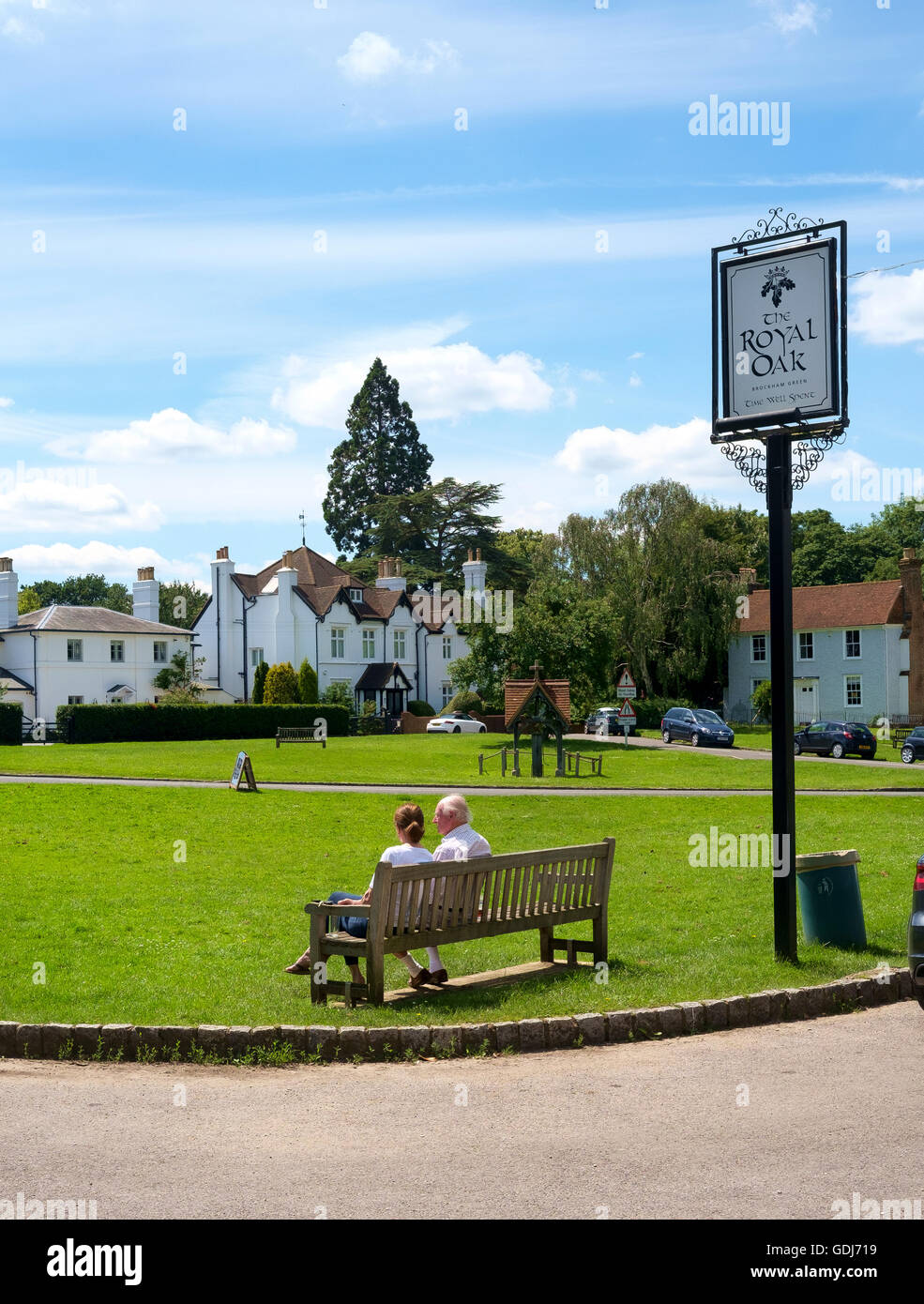 The village green of Brockham, Surrey, UK - a man and a woman sit on a bench outside The Royal Oak pub Stock Photo