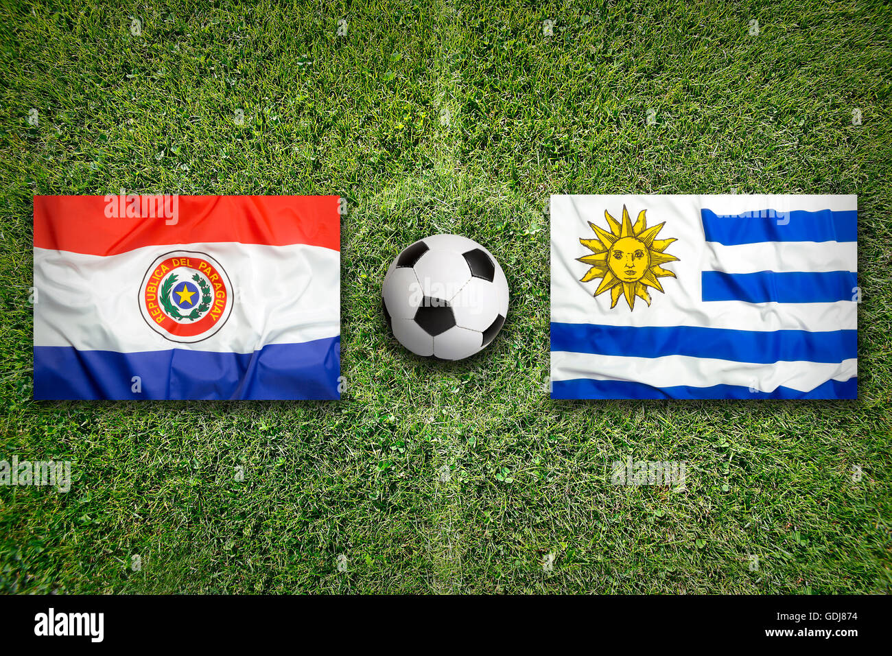 Paraguay vs. Uruguay flags on green soccer field Stock Photo
