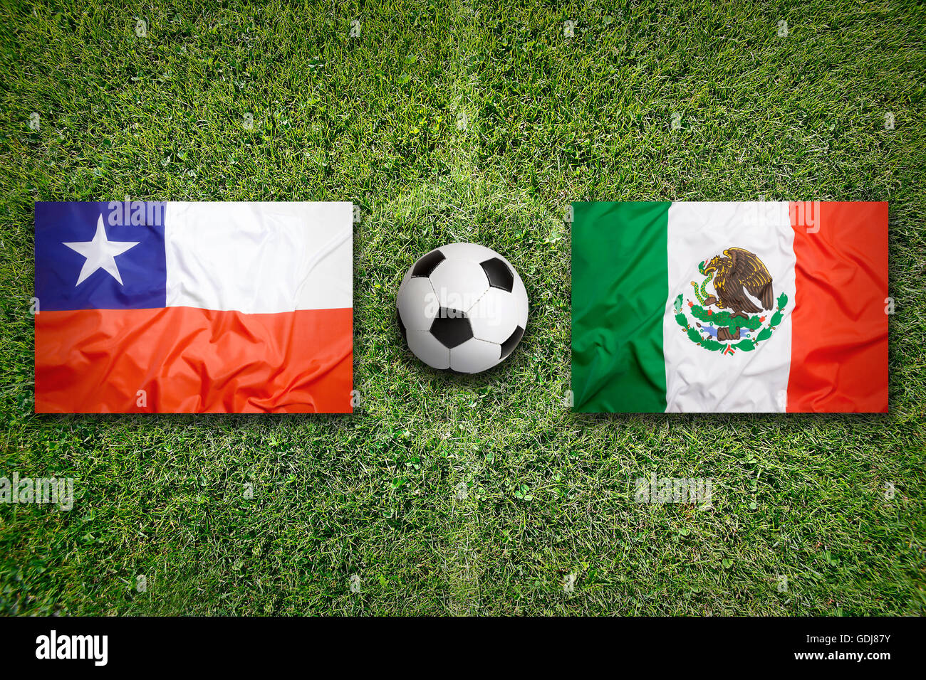 Chile vs. Uruguay flags on green soccer field Stock Photo