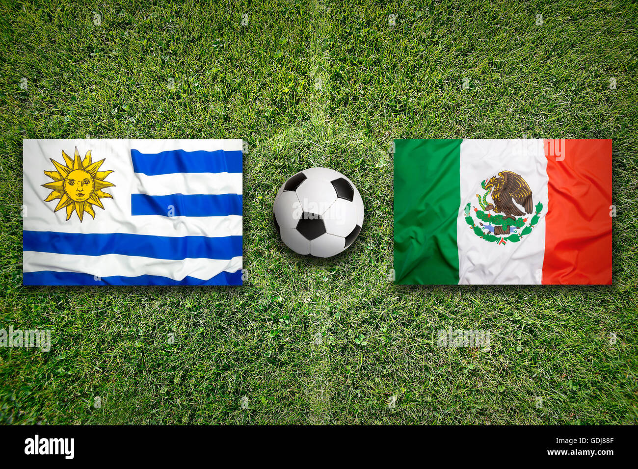 Uruguay vs. Mexico flags on green soccer field Stock Photo