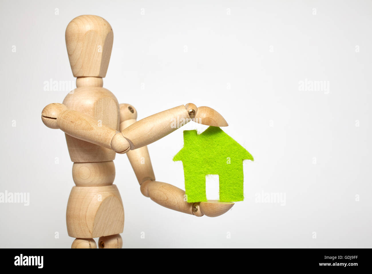 Wooden puppet holds small green house on white background Stock Photo