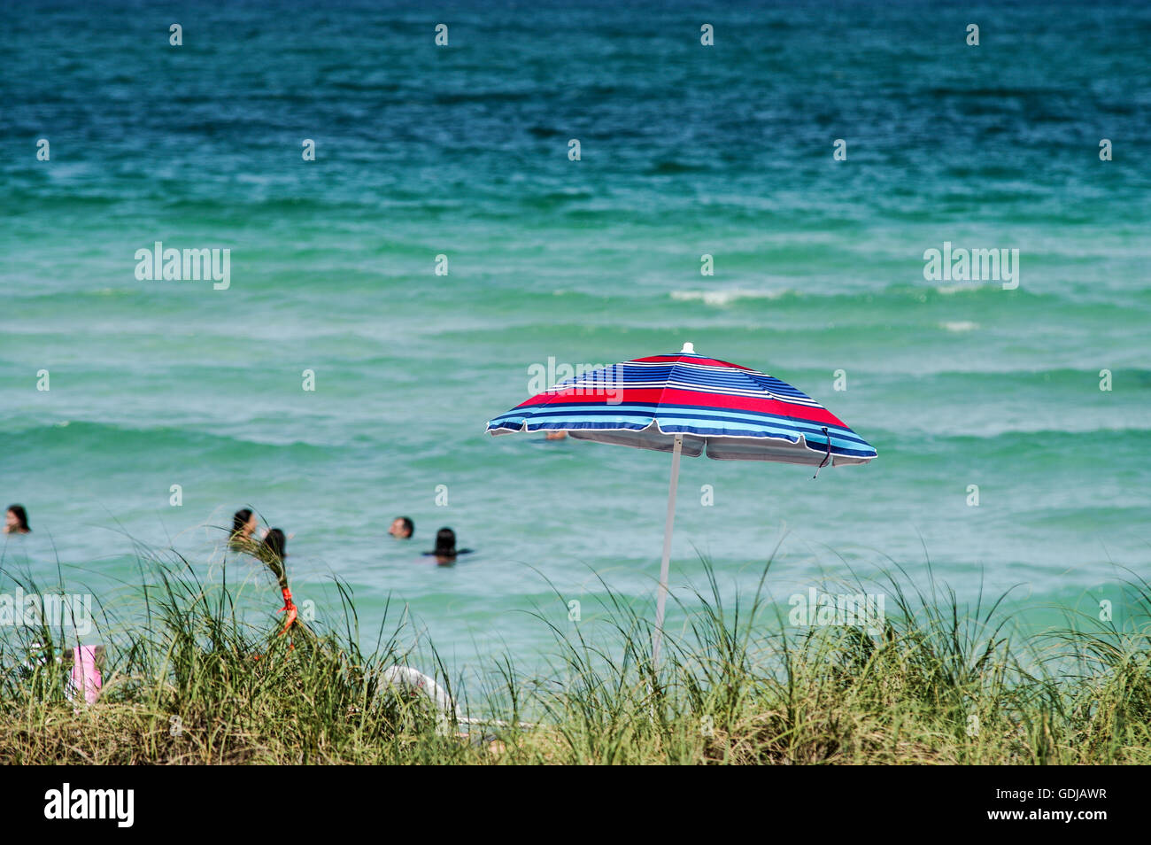 Blue and red umbrella with the ocean and bathers in the background - South Beach in Miami Stock Photo