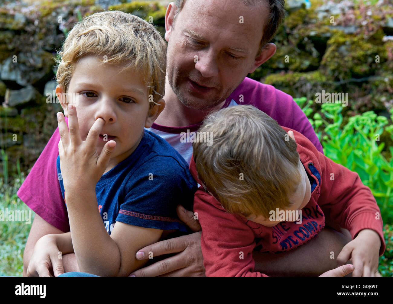Man and two sons, aged two and five... one of them picking his nose Stock Photo