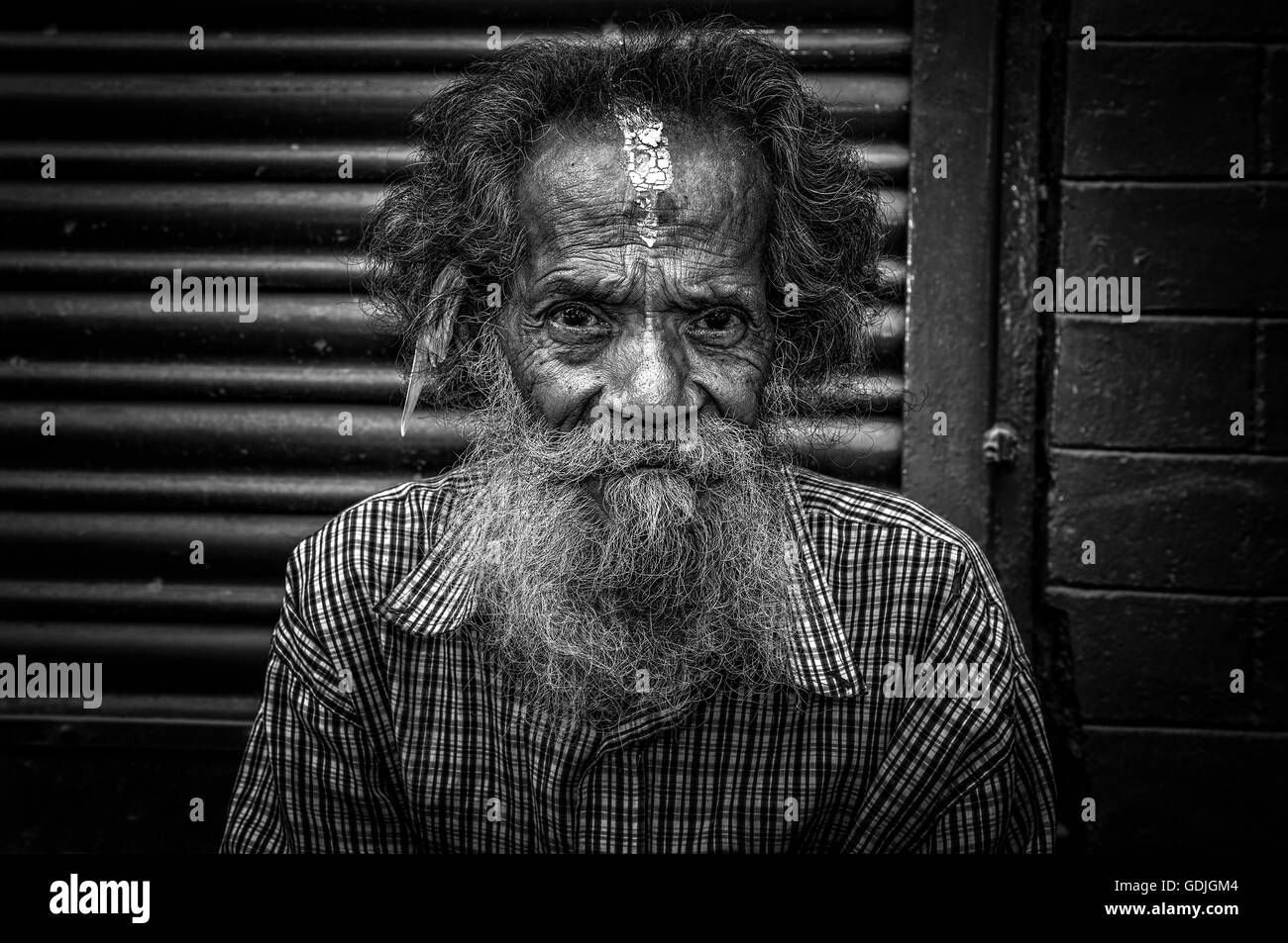 Black and white portrait of an old man sitting in the street of Kathmandu Stock Photo